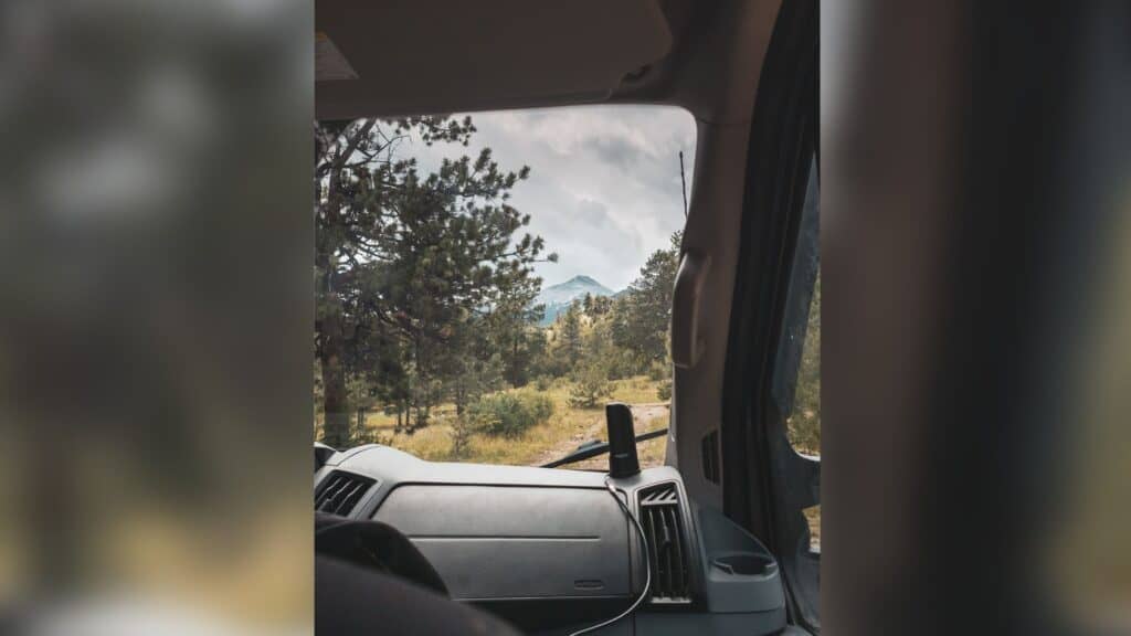 Looking out through the windshield on the passenger side of a ford transit van. The passenger seat is visible slightly in the lower left of the fram. The view is of a mountain in the distance. Living in a van.