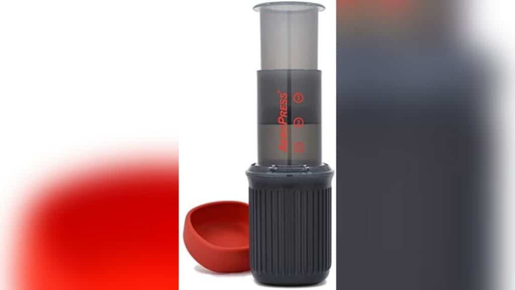 An Aeropress go that is put together with the red lid top next to it.