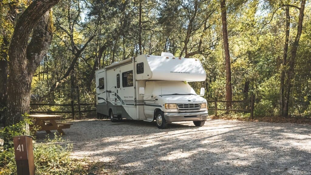 Winnebago class C RV parked on a gravel pad in the woods at a state parks. 