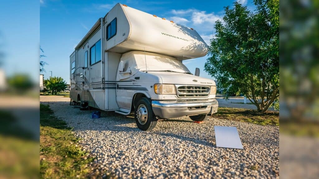 Class C RV parked on white gravel. In front of the RV is a white Starlink Dish Sitting in the ground.